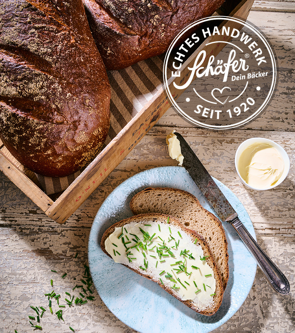 Scheibe Roggenmischbrot mit Butter und Schnittlauch auf einem blauen Teller.