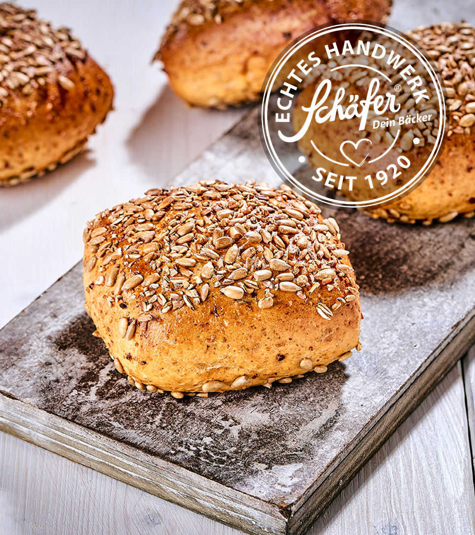 Kerniges Fitnessbrötchen mit Körnermix auf Holzbrett, echtes Handwerk seit 1920.