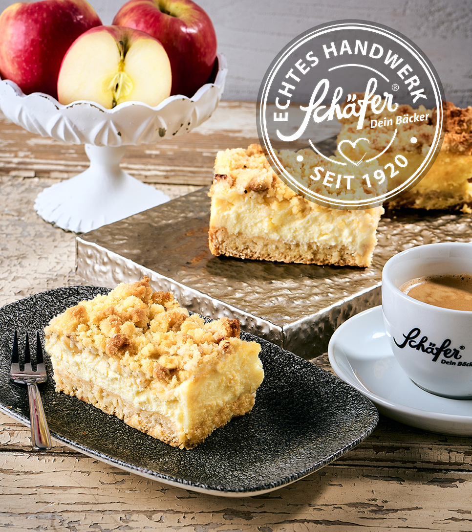 Stück Apfel-Schmand-Kuchen mit Streuseln neben Kaffee und Äpfeln
