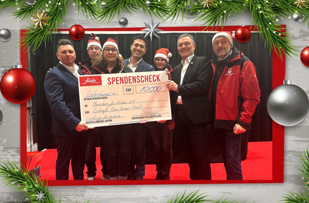 Spendenübergabe mit Scheck über 10.000 € beim Tannenbaumfest, Gruppe mit Weihnachtsmützen.